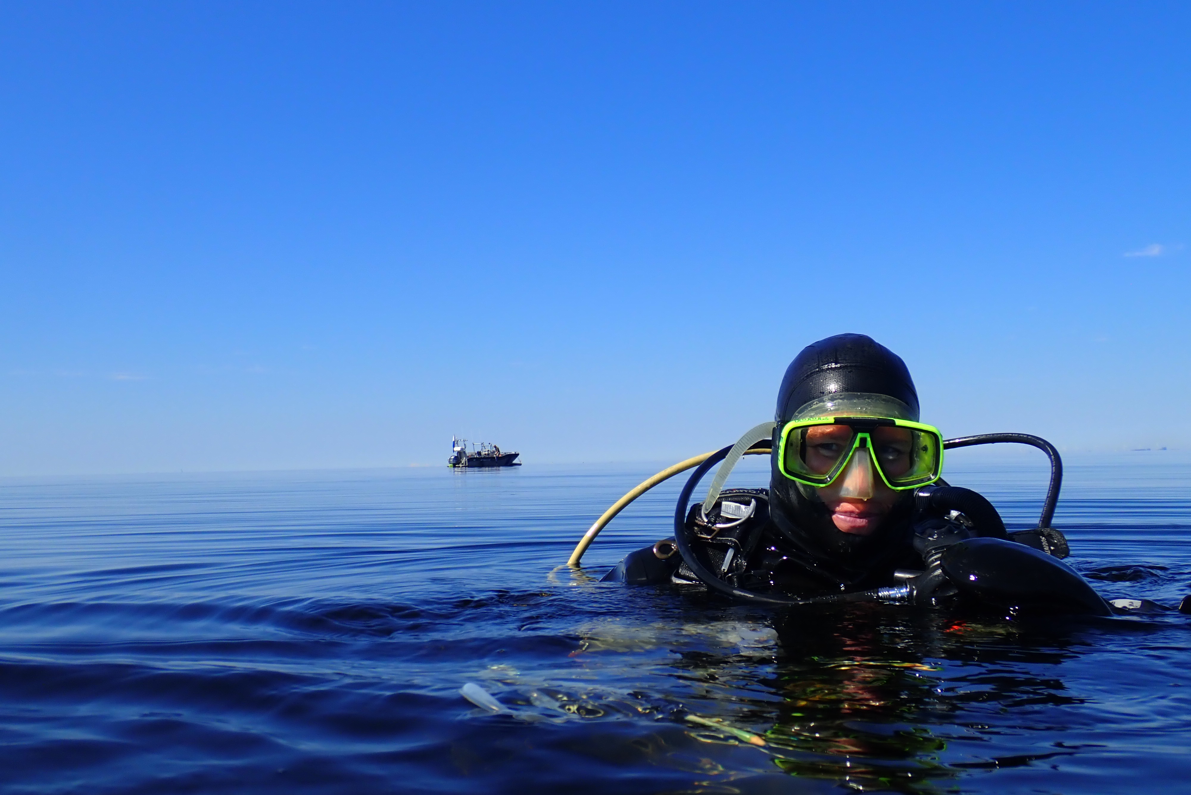 A diver floats on the surface with the support boat in the background.