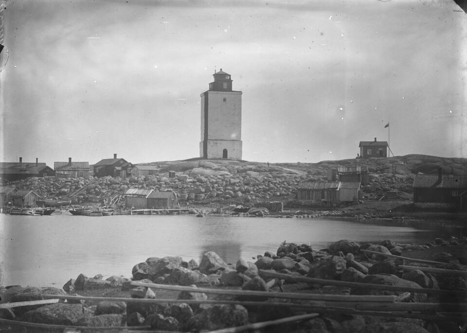 Vanha mustavalkoinen kuva majakasta kallioisella meren saarella, edessä tyyni merenlahti.