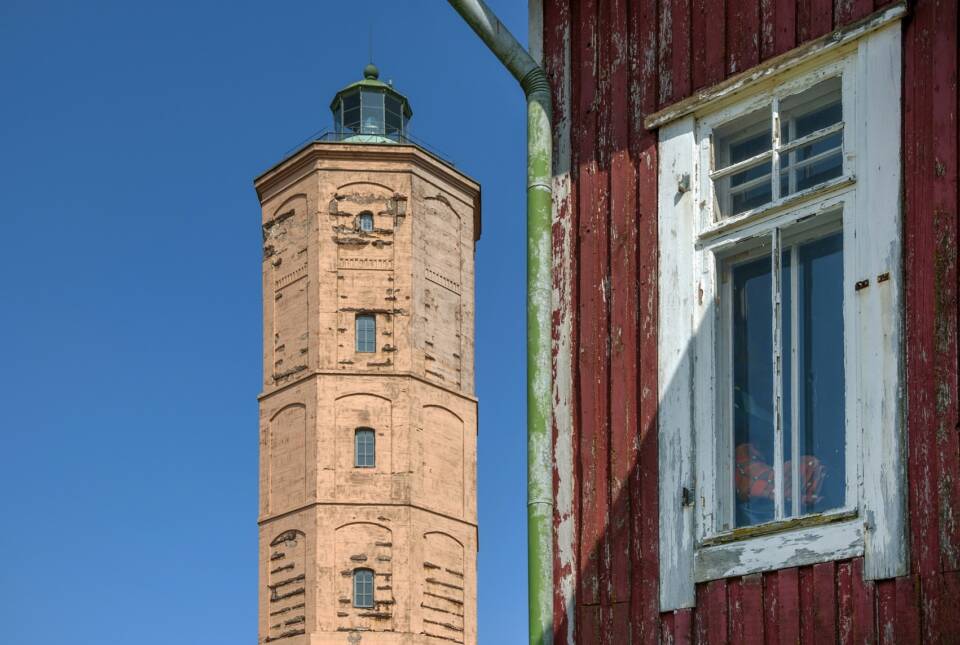 Majakka ja punamultaisen puurakennuksen nurkka kirkkaansinistä taivasta vasten.