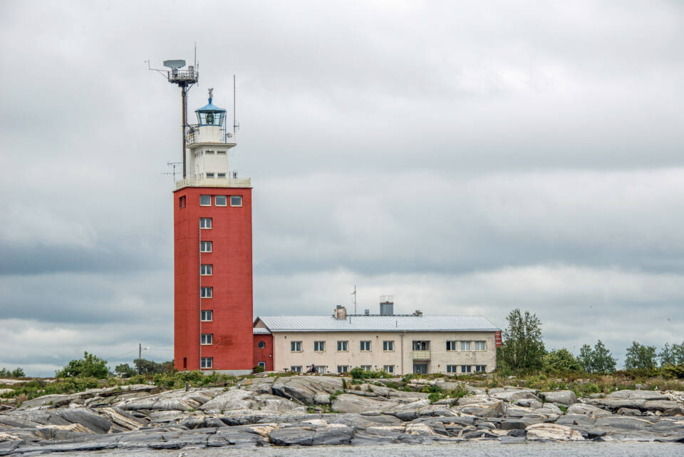 Majakka, jonka toisella puolella on myös matala rakennus, kalliota ja matalia lehtipuita.