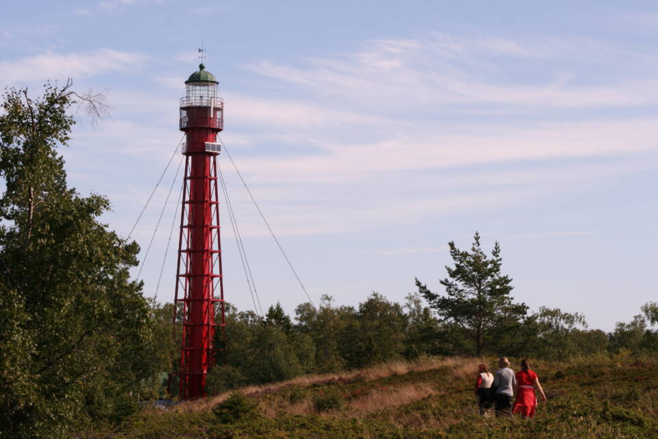 Kolme henkilöä menossa kohti metsänreunassa seisovaa rautamajakkaa iltaruskossa.