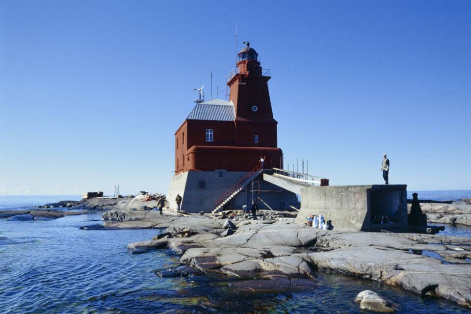 Pieni, neliskanttinen, punainen majakkarakennus jykevällä betonijalustalla pikkuruisella kallioluodolla.