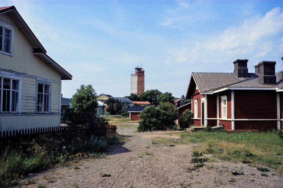 Eri värisiä taloja kylänraitilla, taustalla siintää majakka.