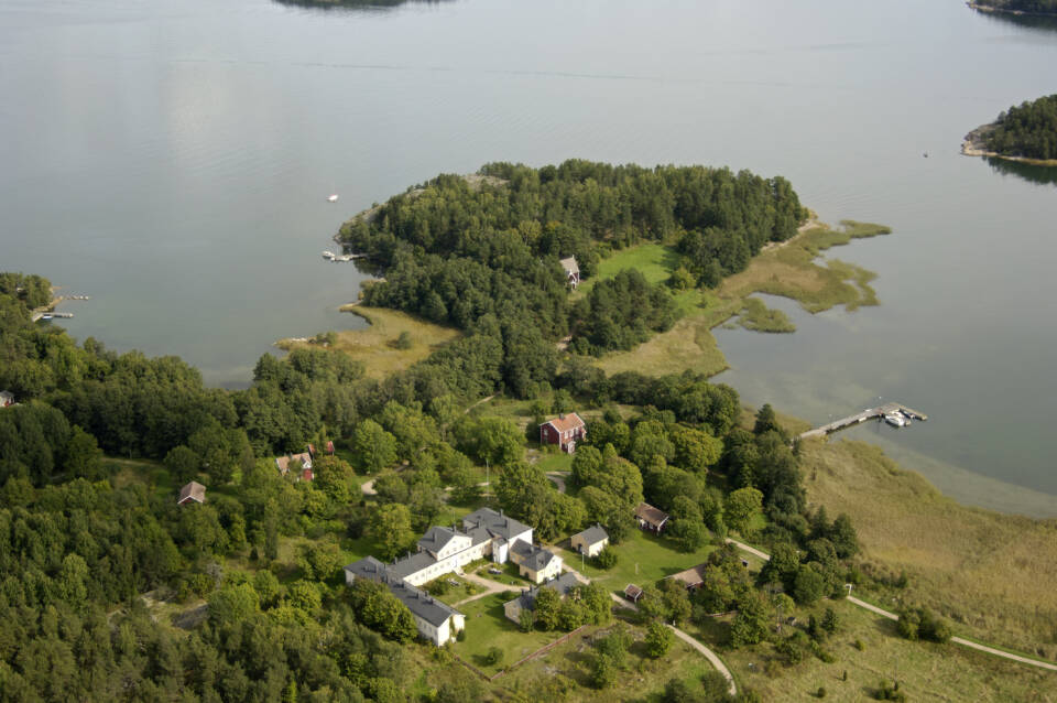 Erilaisia rakennuksia metsän keskellä melkein niemessä, ympärillä tyyntä merta ilmasta katsottuna.