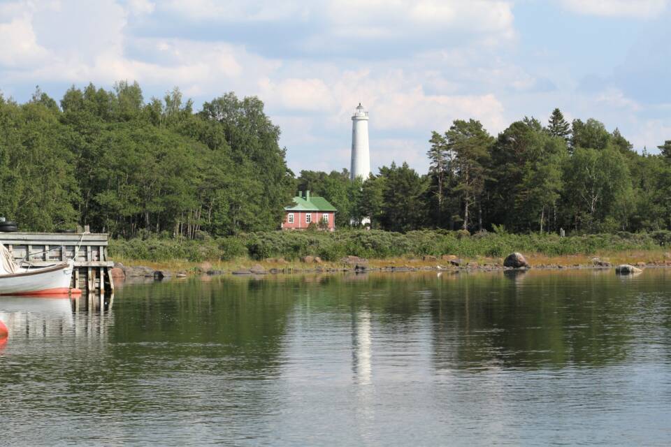 Yksivärinen majakka pilkottaa esiin lehtipuiden joukosta.