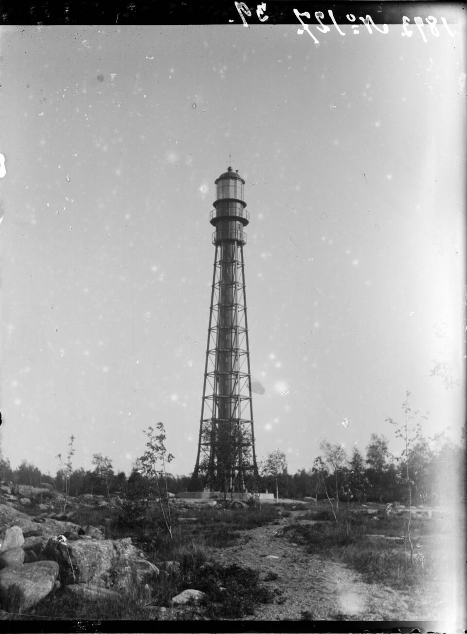 Mustavalkoinen ja hieman huonokuntoinen kuva rautatornista karussa, matalapuustoisessa kivikkomaisemassa.